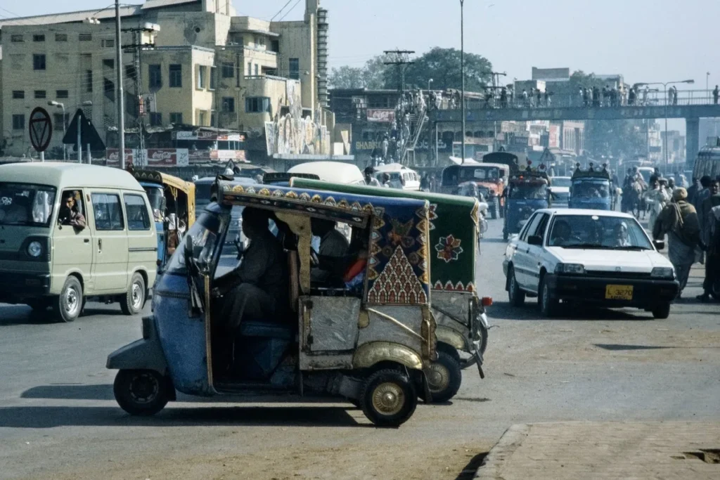 Un rickshaw y coches en una calle urbana de Pakistán.