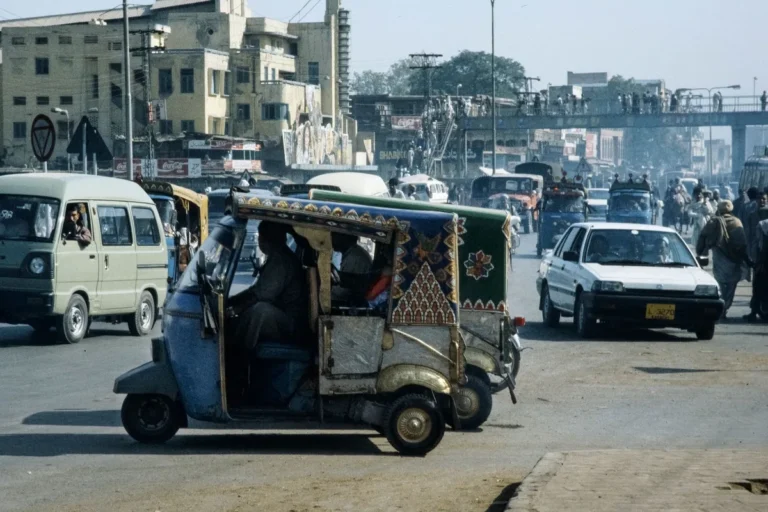 Rickshaw and cars on an urban road in Pakistan.