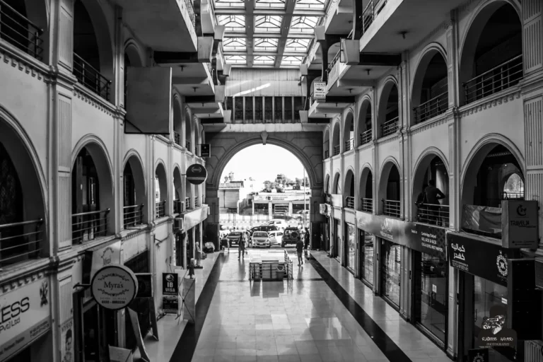 Black and white view down an arcaded shopping mall corridor with shopfronts on two levels in Peshawar.