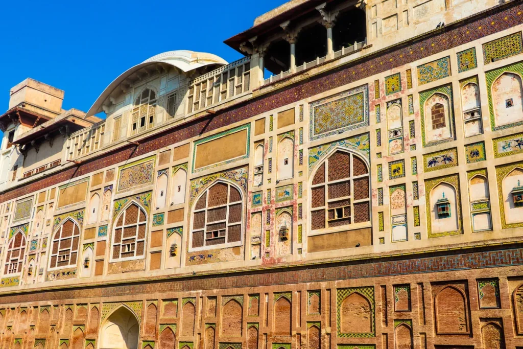 Colourful tile-mosaic panels covering the long Picture Wall of Lahore Fort under a clear blue sky.