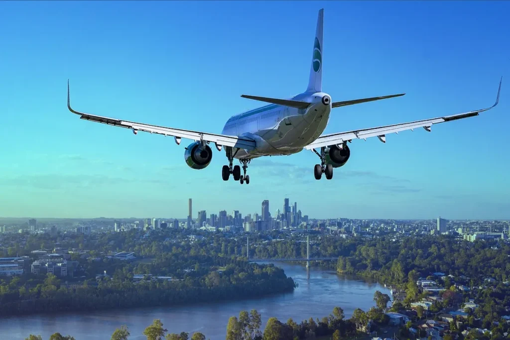 A passenger jet on final approach with its landing gear down, flying above a river and a city skyline.