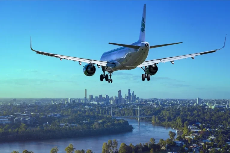 A passenger jet on final approach with its landing gear down, flying above a river and a city skyline.