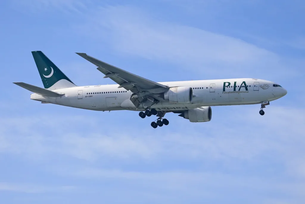 A Pakistan International Airlines Boeing 777 flying against a clear blue sky with its landing gear down.