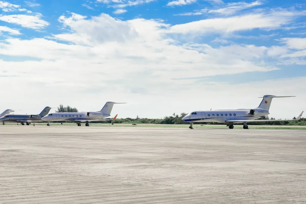 Several private business jets parked on an open airport apron under a bright, partly cloudy sky.