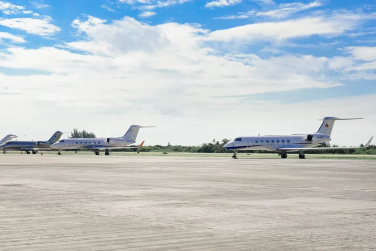 Several private business jets parked on an open airport apron under a bright, partly cloudy sky.