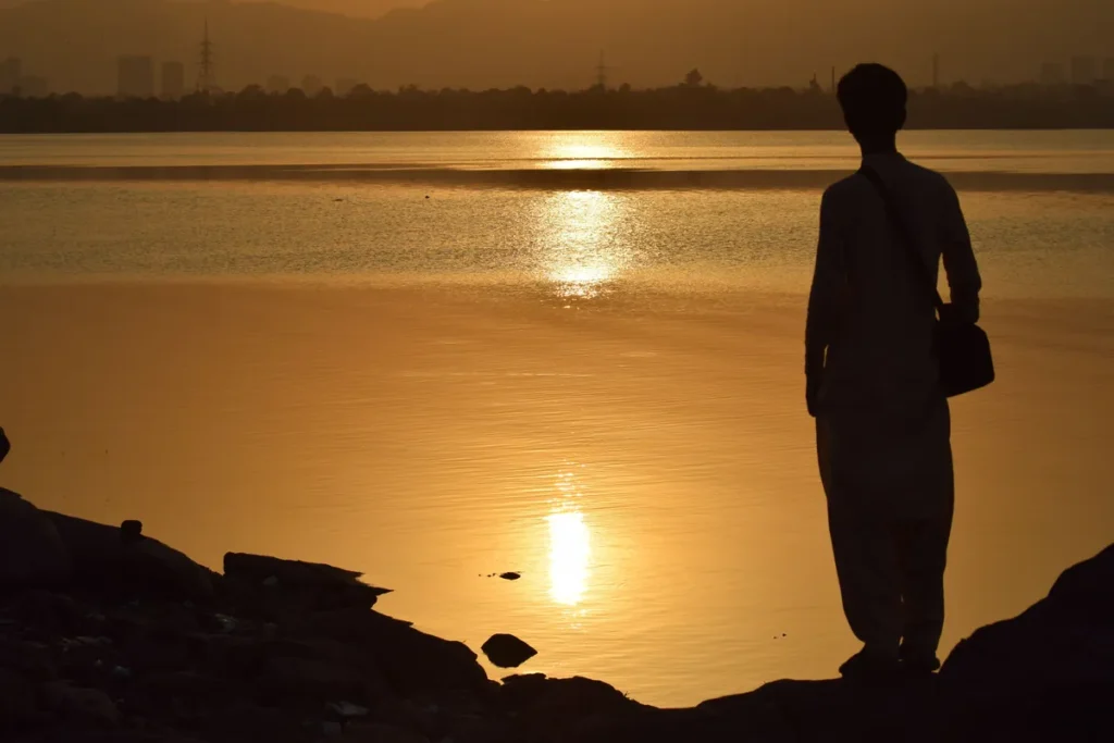 A man silhouetted against a golden sunset reflected in a calm lake in Islamabad, Pakistan.